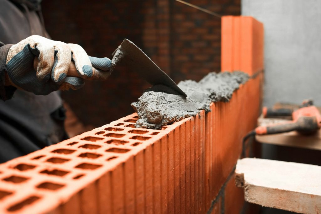 Bricklayer puts bricks to make a wall