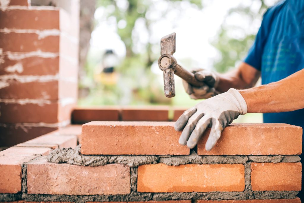 industrial worker building exterior walls, using hammer for laying bricks in cement